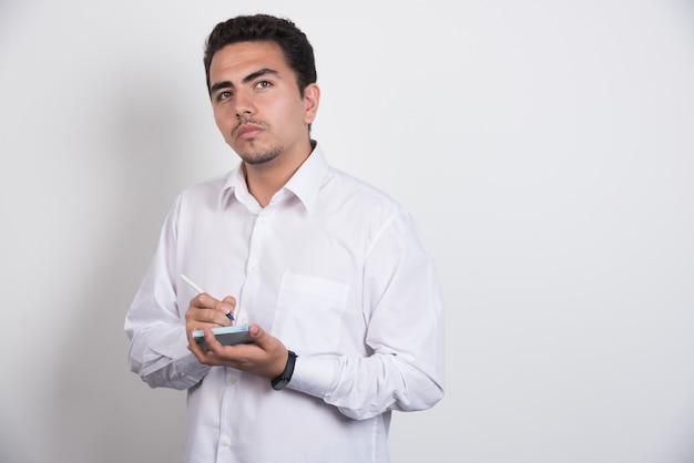 Joven empresario escribiendo sobre fondo blanco.