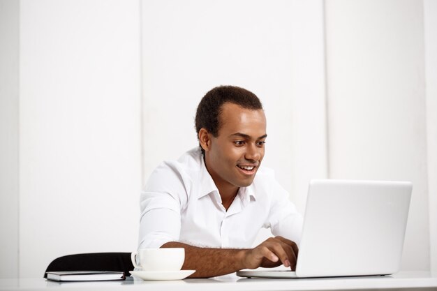 Joven empresario exitoso escribiendo en la computadora portátil, sentado en el lugar de trabajo