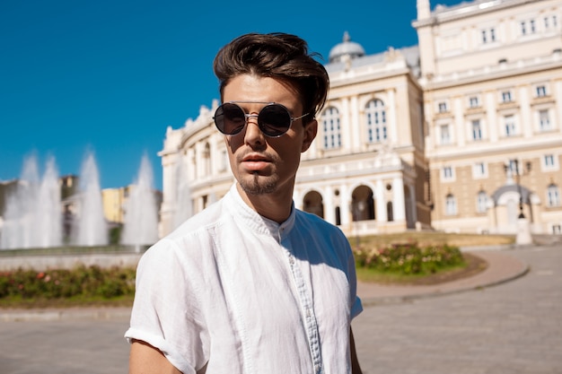 Joven empresario exitoso en gafas de sol caminando por la ciudad soleada.