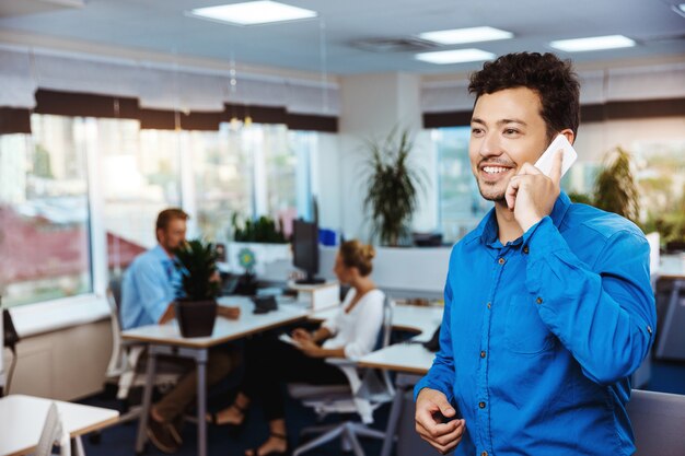 Joven empresario exitoso hablando por teléfono, sonriendo, sobre la oficina