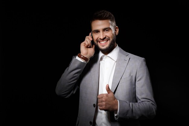 Joven empresario exitoso sonriendo hablando por teléfono sobre fondo negro