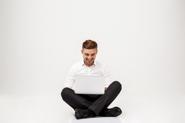 Joven empresario exitoso sonriendo, sentado con el portátil.