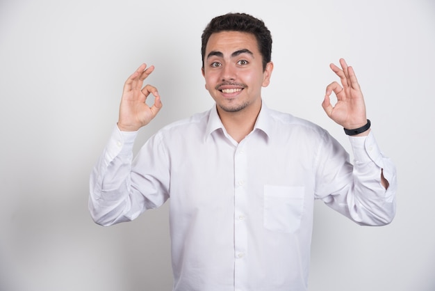 Joven empresario haciendo signo ok sobre fondo blanco.