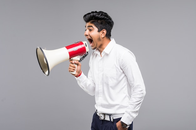 Joven empresario indio anunciando en un megáfono en pared gris