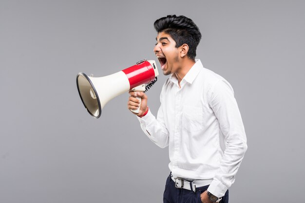 Joven empresario indio anunciando en un megáfono en pared gris