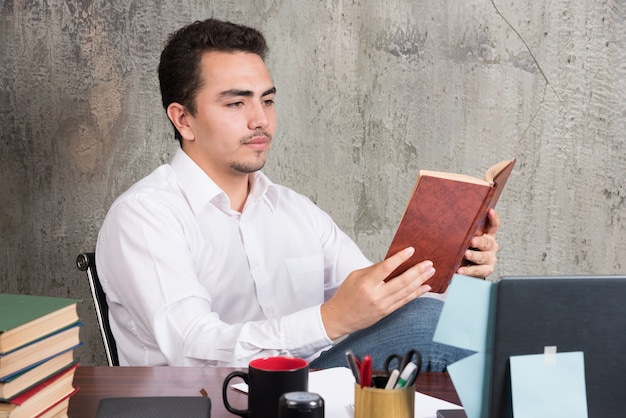 Joven empresario leyendo un libro en el escritorio.