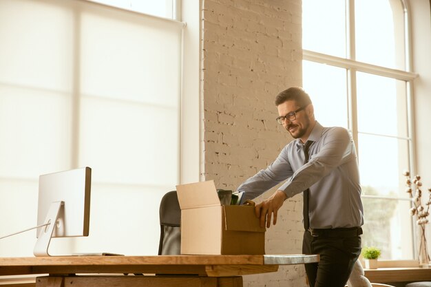 Un joven empresario moviéndose en la oficina, consiguiendo un nuevo lugar de trabajo. Oficinista masculino caucásico joven equipa nuevo gabinete después de la promoción. Se ve feliz. Negocio, estilo de vida, concepto de nueva vida.