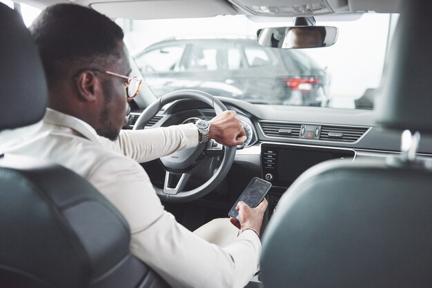 Joven empresario negro prueba de conducir un coche nuevo. Rico hombre afroamericano.