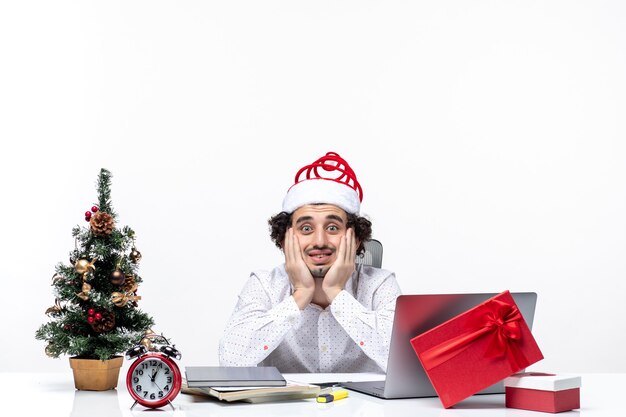 Joven empresario ocupado con divertido sombrero de santa claus posando para la cámara en la oficina sobre fondo blanco.