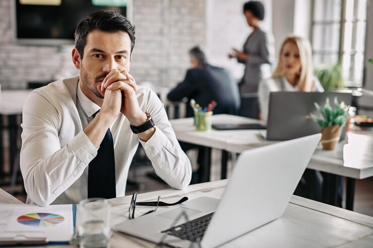 Foto gratuito joven empresario pensativo trabajando en el escritorio de la oficina y pensando en algo hay gente en el fondo