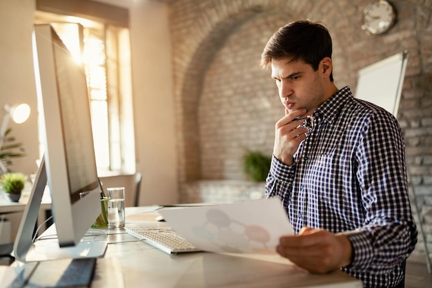 Joven empresario preocupado leyendo informes de negocios mientras trabaja en la oficina