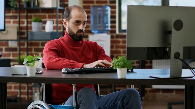 Joven empresario que usa computadora para crear gráficos de datos, trabajando en una oficina adaptada para discapacitados. Trabajador masculino con estadísticas de marketing de planificación de discapacidad en conexión a Internet, trabajo ejecutivo.