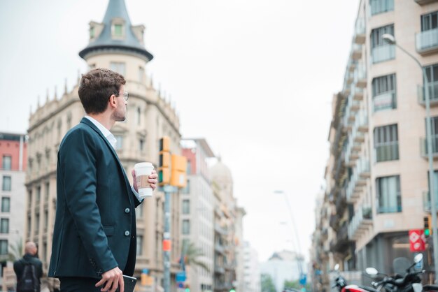 Joven empresario sosteniendo una taza de café en la mano mirando edificios en la ciudad