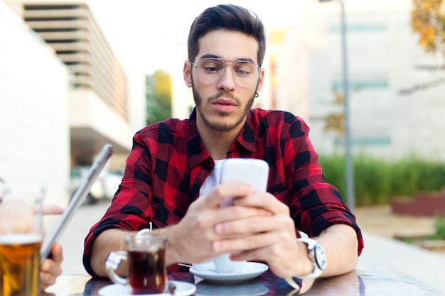 Foto gratuita joven empresario usando su teléfono móvil en la cafetería.