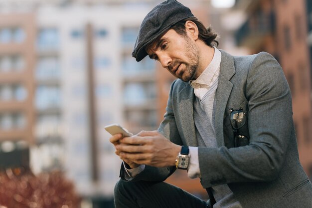 Joven empresario usando teléfono celular y leyendo mensajes de texto en la calle