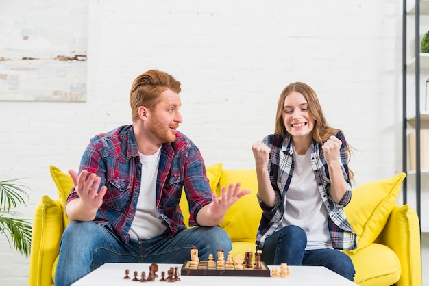 Joven encogiéndose de hombros y mirando a la novia apretando su puño con éxito después de ganar el juego de ajedrez