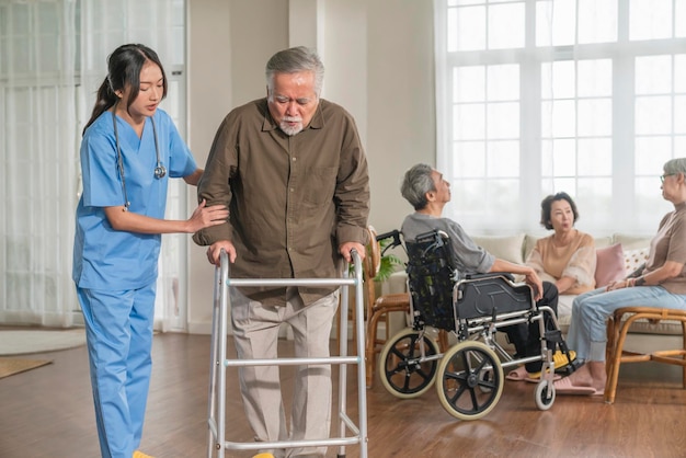 Joven enfermera asiática cuidadora que ayuda a un anciano asiático con andador de movilidad en la sala de estar de la guardería para ancianos.