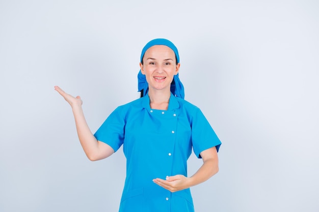 Una joven enfermera sonriente apunta a la izquierda con la mano en el fondo blanco