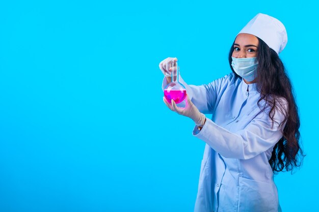 Joven enfermera en uniforme aislado mostrando frasco químico, vista de perfil.