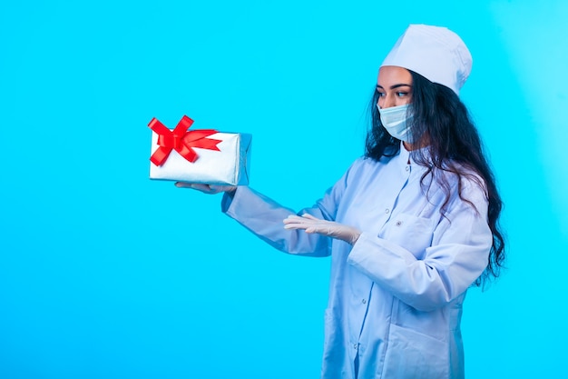 Joven enfermera en uniforme aislado sosteniendo una caja de regalo con cinta roja y presentándola