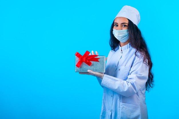 Joven enfermera en uniforme aislado sosteniendo una caja de regalo con cinta roja