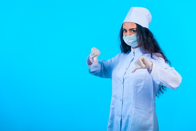 Joven enfermera en uniforme aislado sosteniendo haciendo pulgar hacia abajo signo de mano