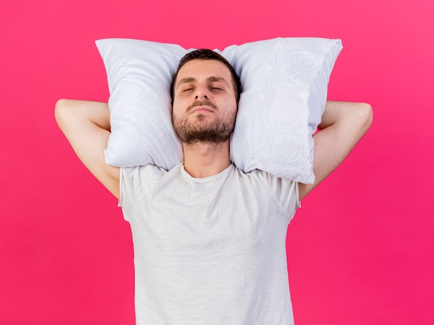 Joven enfermo poniendo almohada detrás de la cabeza aislado en rosa