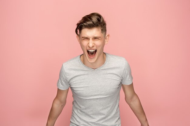 El joven enojado emocional gritando en espacio de estudio rosa