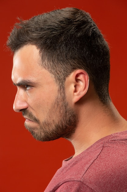 El joven enojado emocional gritando en la pared roja del estudio