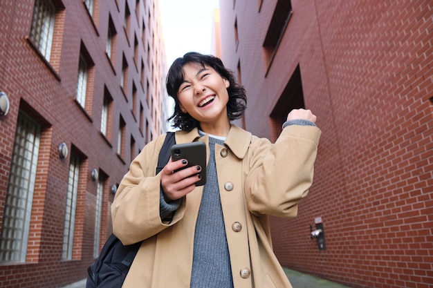 Una joven entusiasta baila en la calle celebra los triunfos de la victoria y sostiene un teléfono inteligente que me lee un mensaje de texto