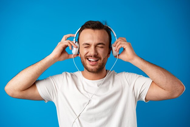Joven escuchando música con auriculares sobre fondo azul.