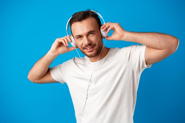 Joven escuchando música con auriculares sobre fondo azul.