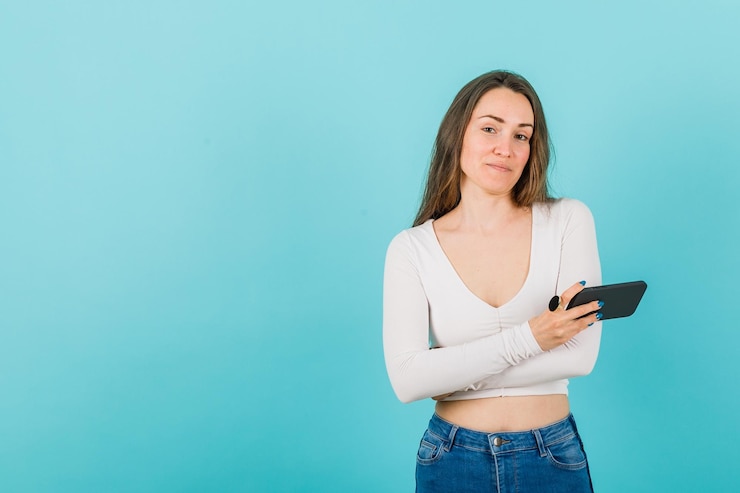 Foto gratuito la joven está cruzando los brazos sosteniendo un teléfono inteligente con fondo azul