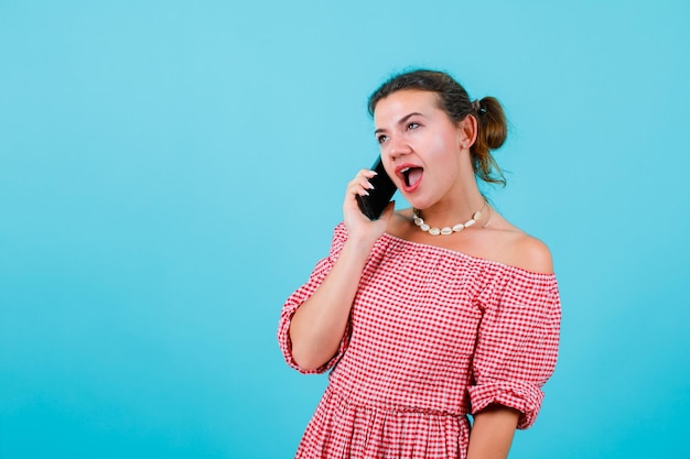 La joven está hablando por teléfono riéndose de fondo azul