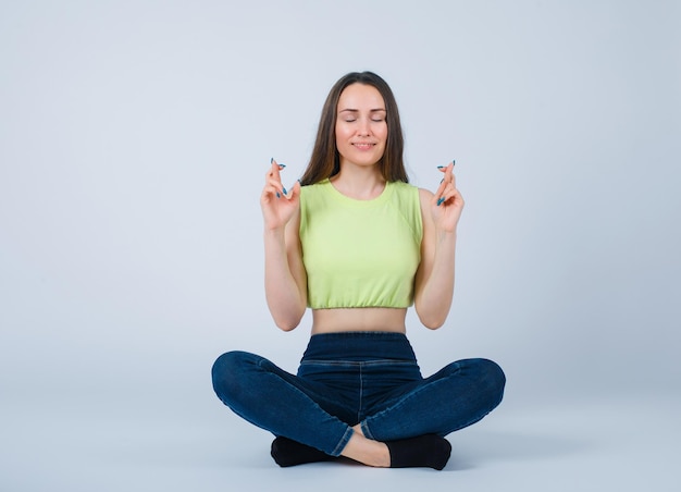 La joven está meditando sentada en el suelo sobre fondo blanco.