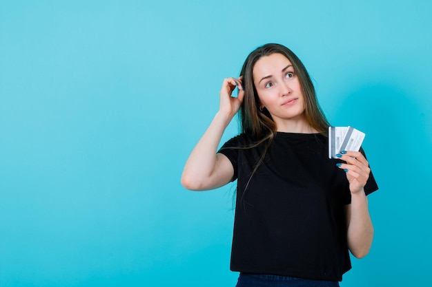 La joven está mirando hacia arriba y sosteniendo tarjetas de crédito con fondo azul.