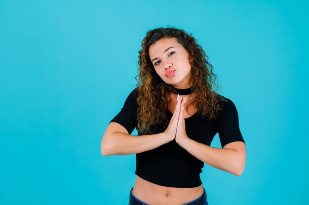 La joven está mostrando un gesto de oración tomándose de la mano en el fondo azul