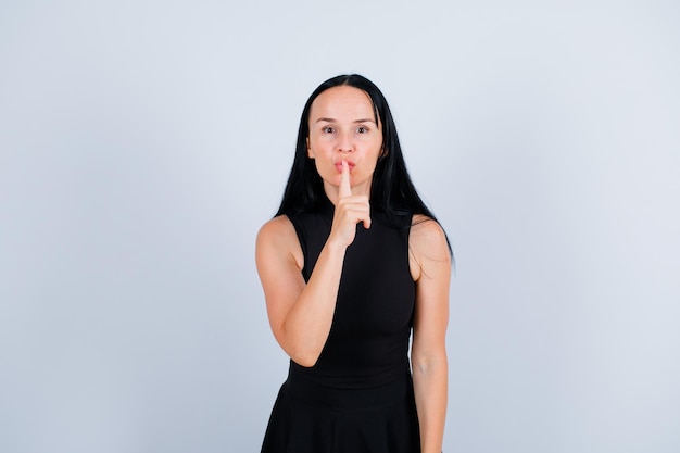 La joven está mostrando un gesto de silencio sosteniendo el dedo índice en los labios sobre fondo blanco.
