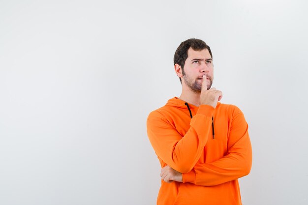 El joven está pensando poniendo su dedo índice en los labios sobre fondo blanco.