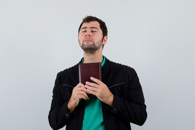 El joven está soñando sosteniendo un cuaderno sobre fondo blanco.