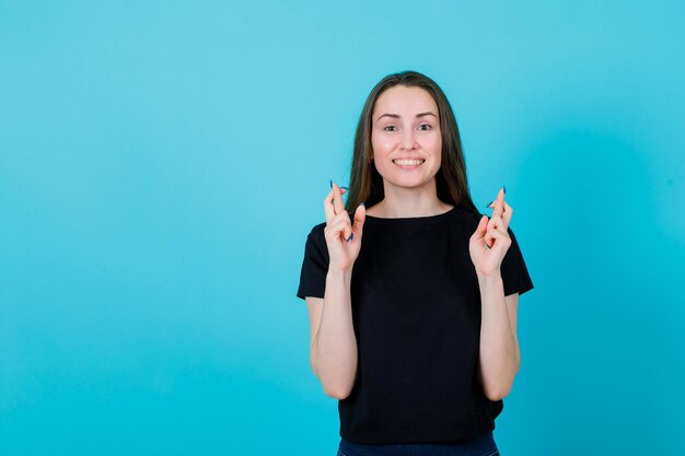 La joven está sonriendo levantando los dedos cruzados sobre fondo azul.