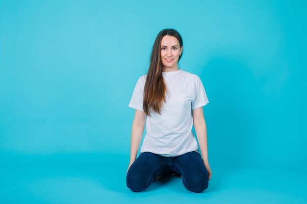 La joven está sonriendo sentada en el suelo sobre fondo azul.