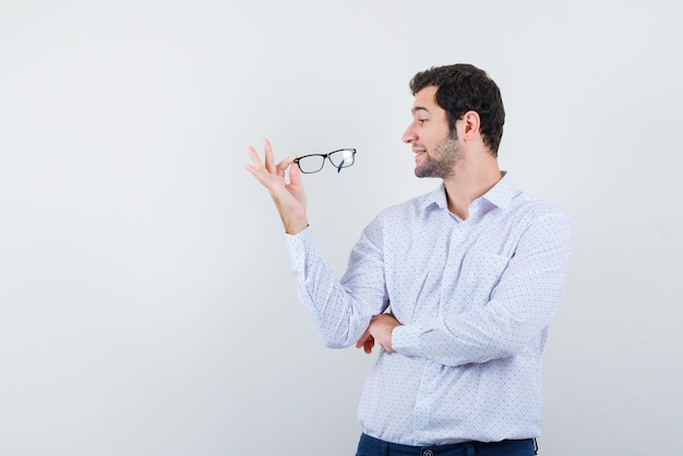 El joven está sosteniendo sus gafas sobre fondo blanco.