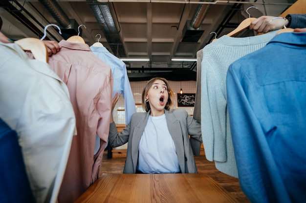 Joven estilista mirando a través de un conjunto de camisas para disparar a la moda