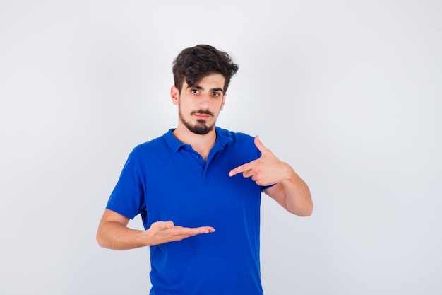 Joven estirando una mano como sosteniendo algo y apuntando con el dedo índice en camiseta azul y mirando serio