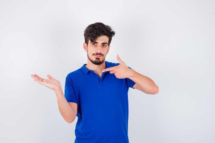 Foto gratuito joven estirando una mano como sosteniendo algo y apuntando con el dedo índice en camiseta azul y mirando serio