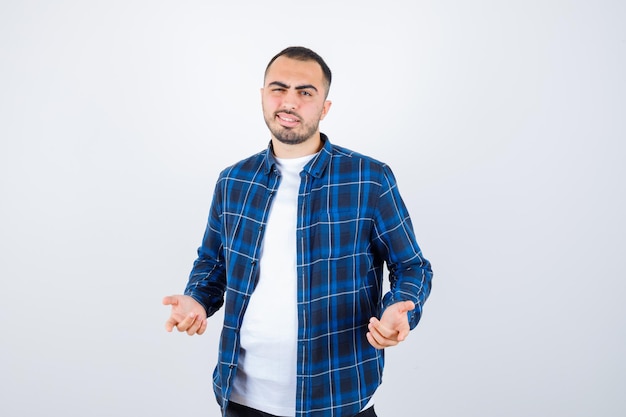 Joven estirando las manos de manera interrogante en camisa a cuadros y camiseta blanca y mirando perplejo