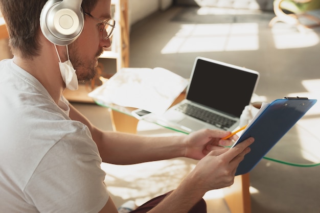 Joven estudiando en casa durante cursos online para jornaleros, periodistas, desarrolladores. Usando computadora portátil, teléfono inteligente, auriculares.