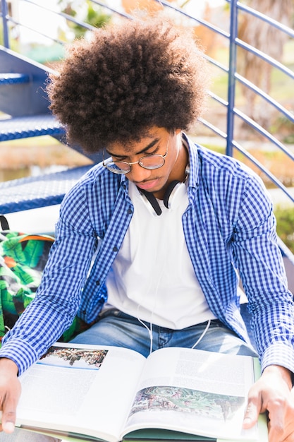 Foto gratuita un joven estudiante afro leyendo el libro al aire libre