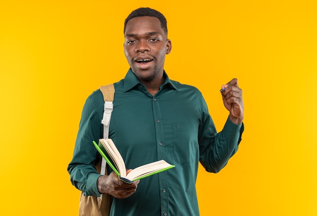 Joven estudiante afroamericano sorprendido con mochila con libro y bolígrafo